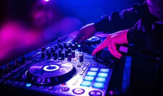 DJ console mixing music hands and with blurred people dancing night club party