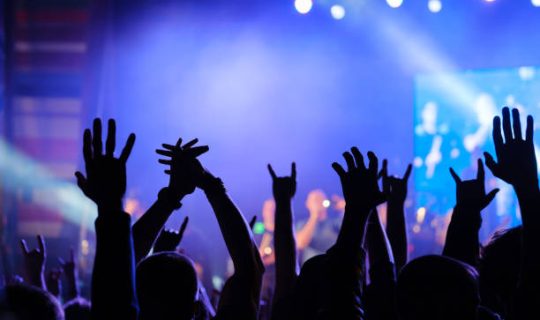 Fans cheering musicians on stage at live rock music concert, back view